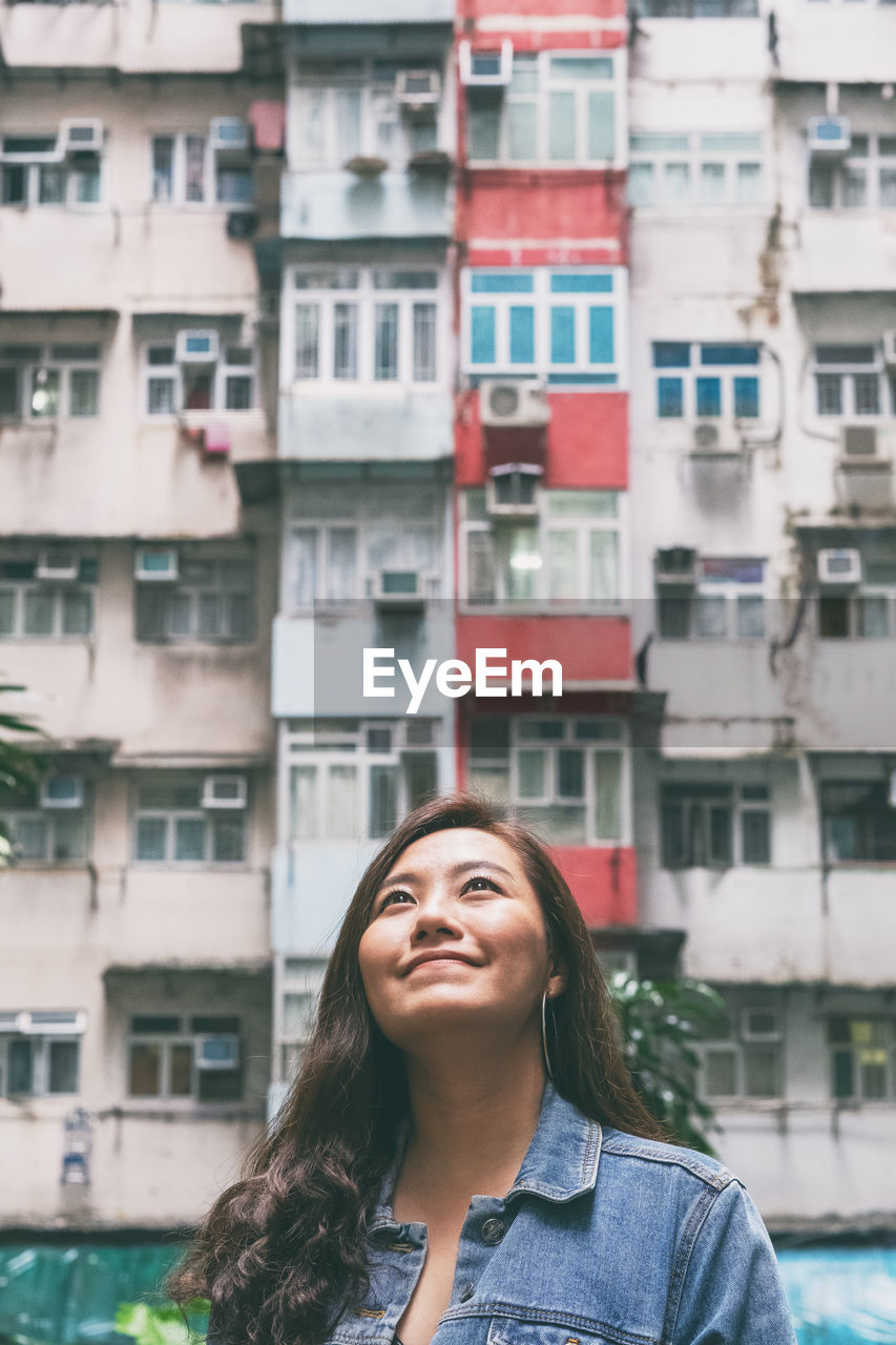 PORTRAIT OF BEAUTIFUL WOMAN STANDING AGAINST RESIDENTIAL BUILDINGS