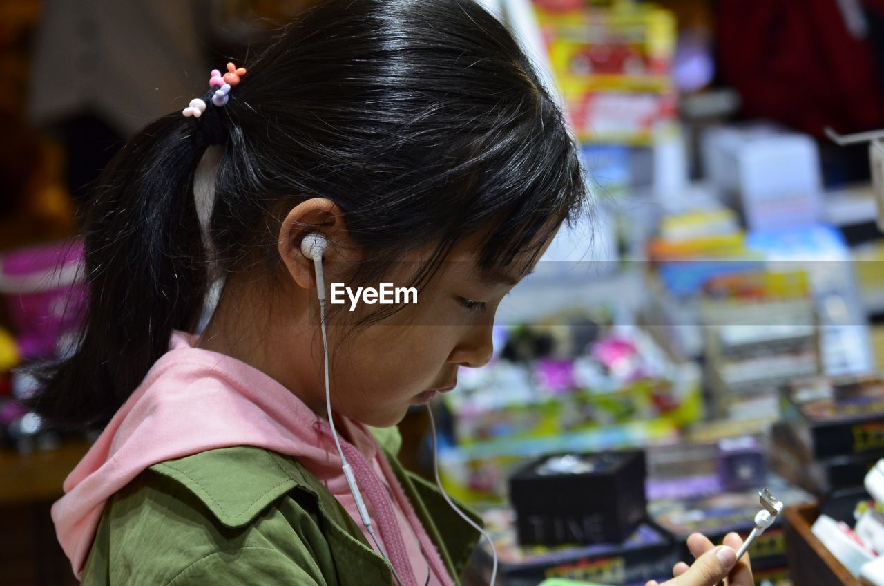 Side view of girl listening music on headphones at store