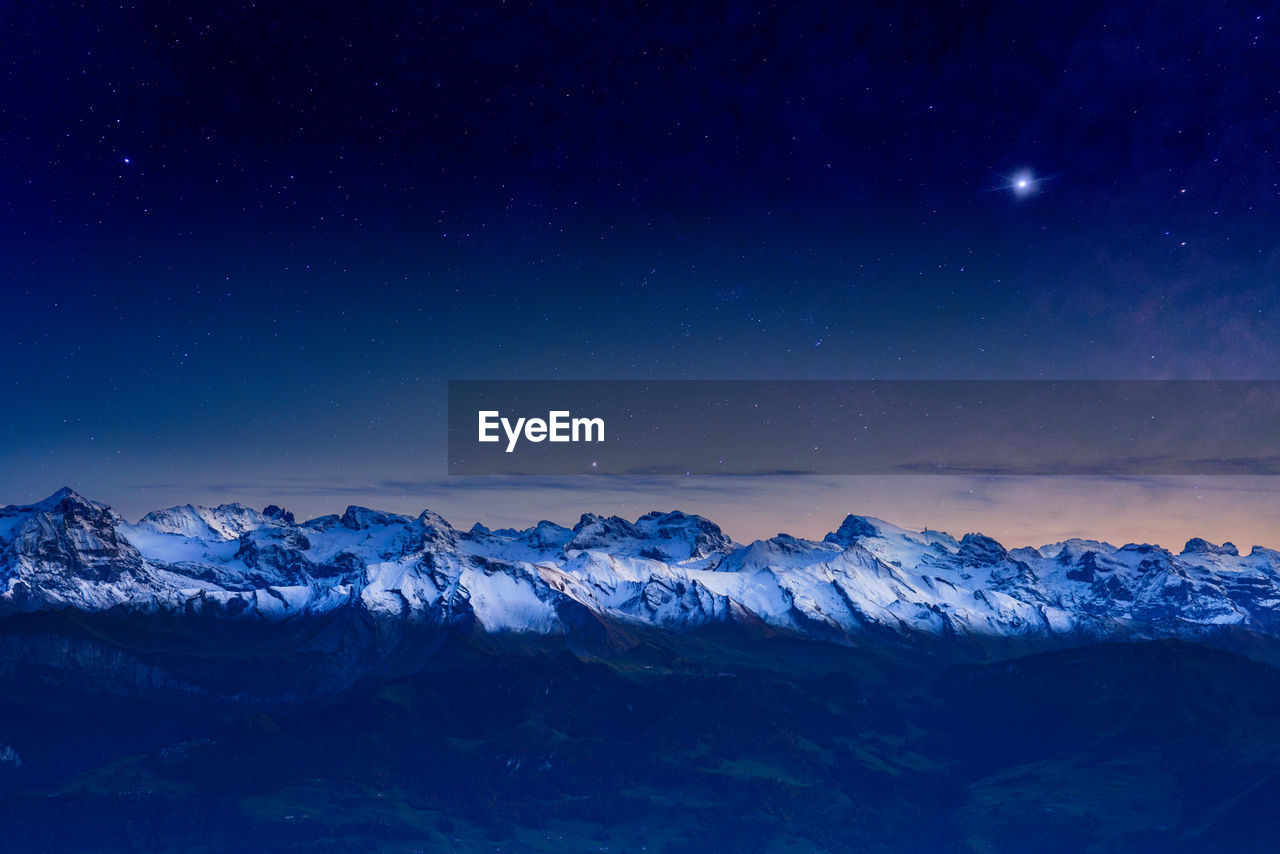 Scenic view of snowcapped mountains against blue sky at night