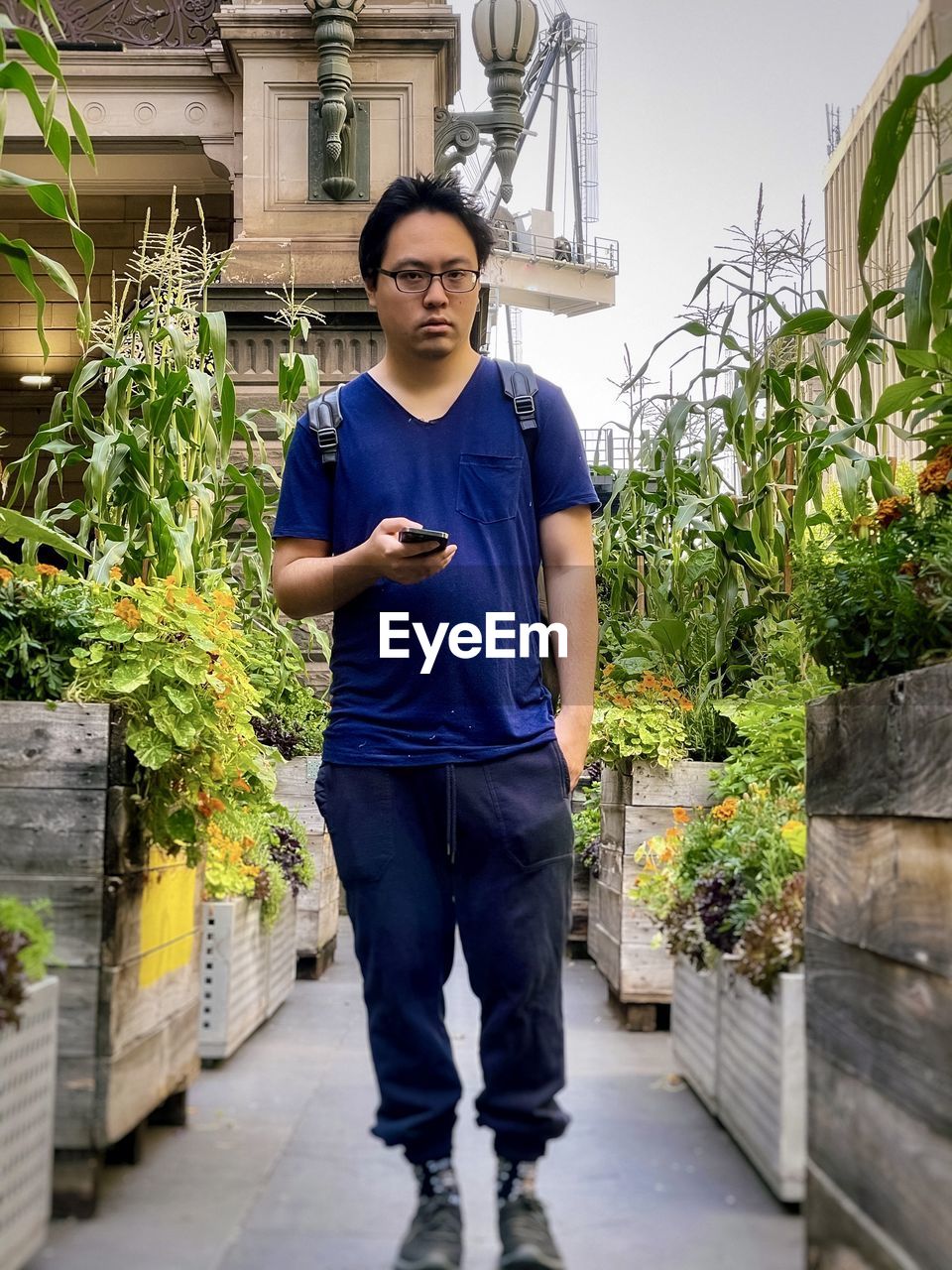 Portrait of young man standing in between flowering plants against buildings in the city.