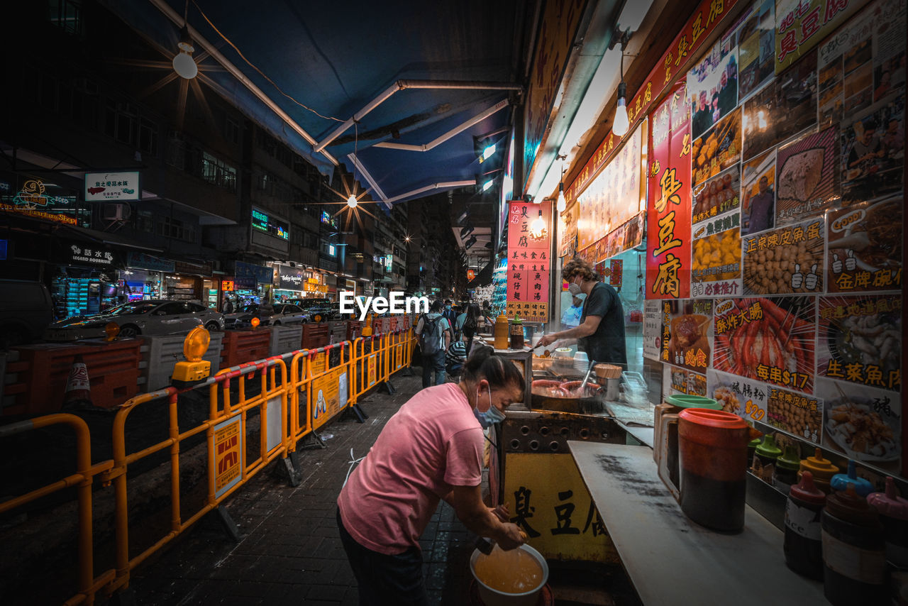 MAN WALKING ON ILLUMINATED STREET MARKET AT NIGHT