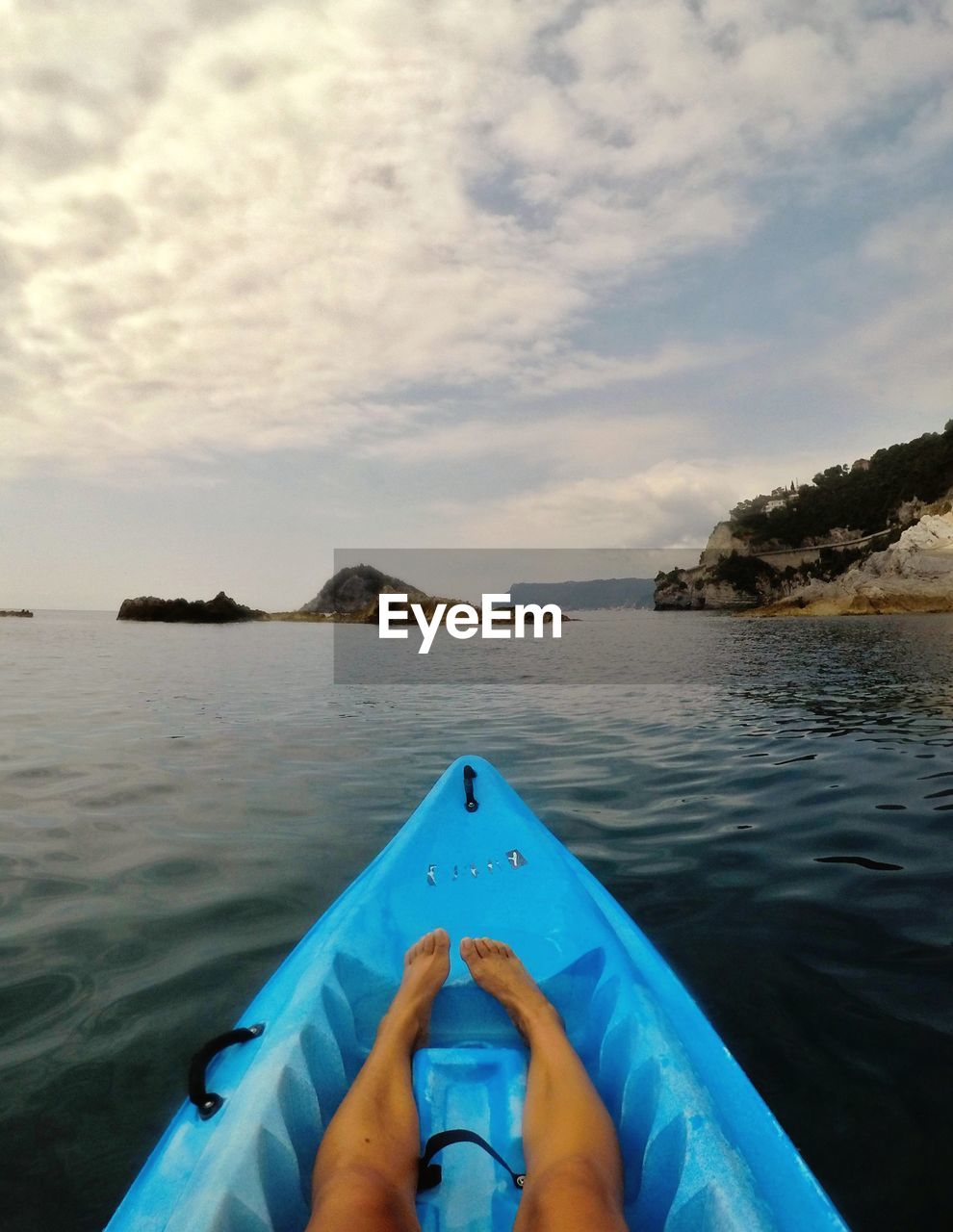 Low section of person relaxing in kayak against cloudy sky
