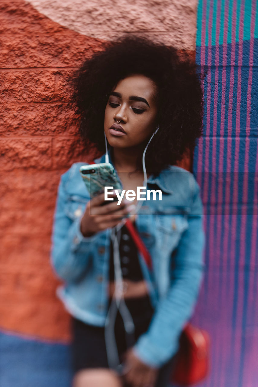 Young woman using mobile phone while standing against wall