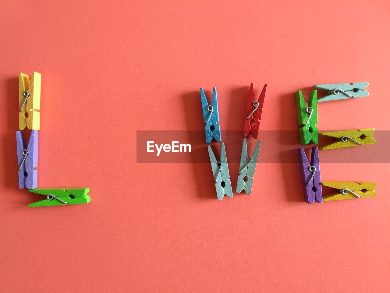 High angle view of colorful wooden clothespins arranged on coral background