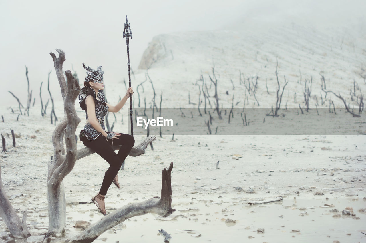 Woman with sword sitting on branch during winter