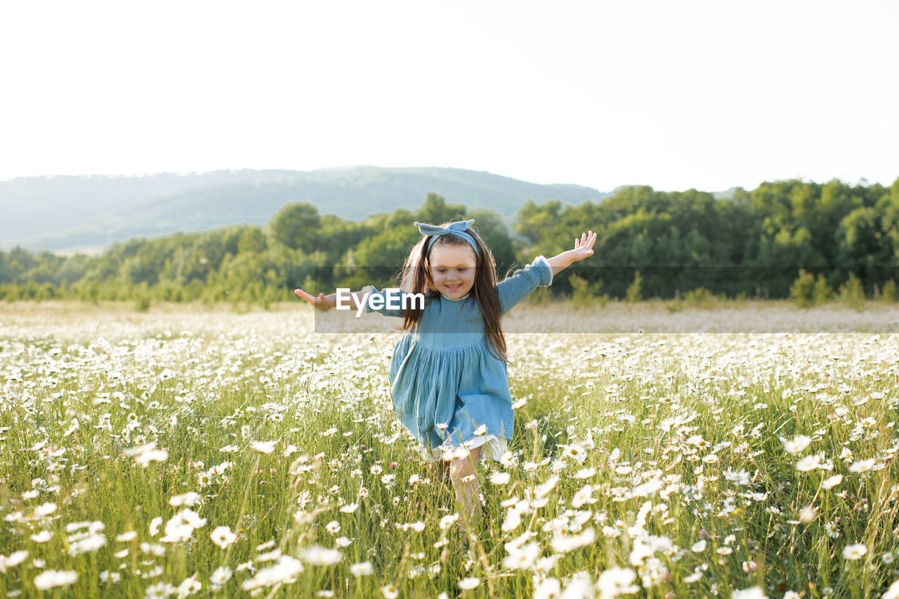 Happy cheerful child girl 3-4 year old wear stylish rustic dress running in meadow with flowers 