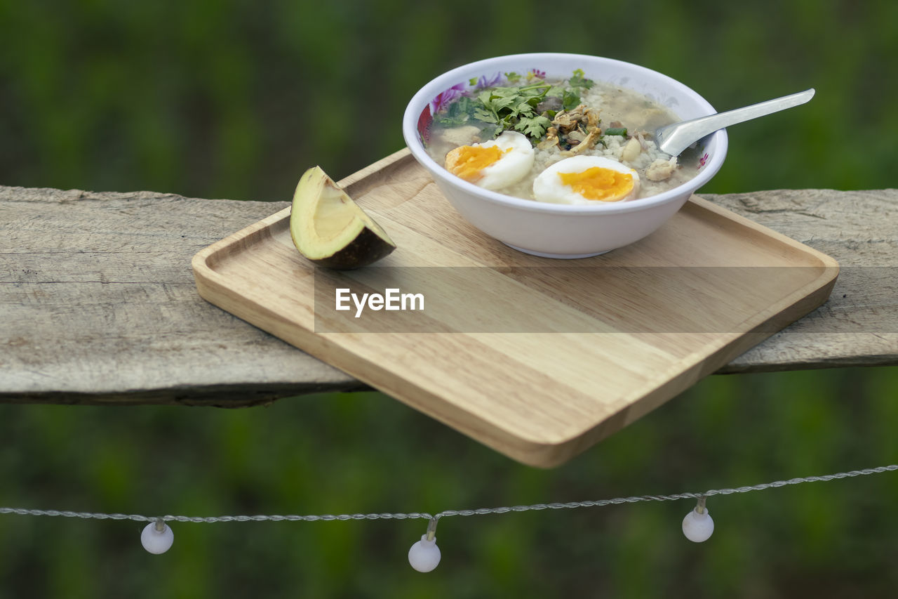 Porridge in a serving bowl with avocado on a wooden tray looks beautiful. 