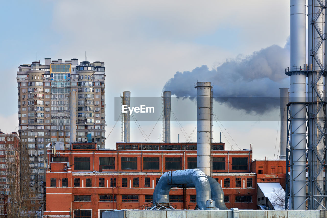 Smoke chimneys from the city thermal station against the background of residential buildings. 