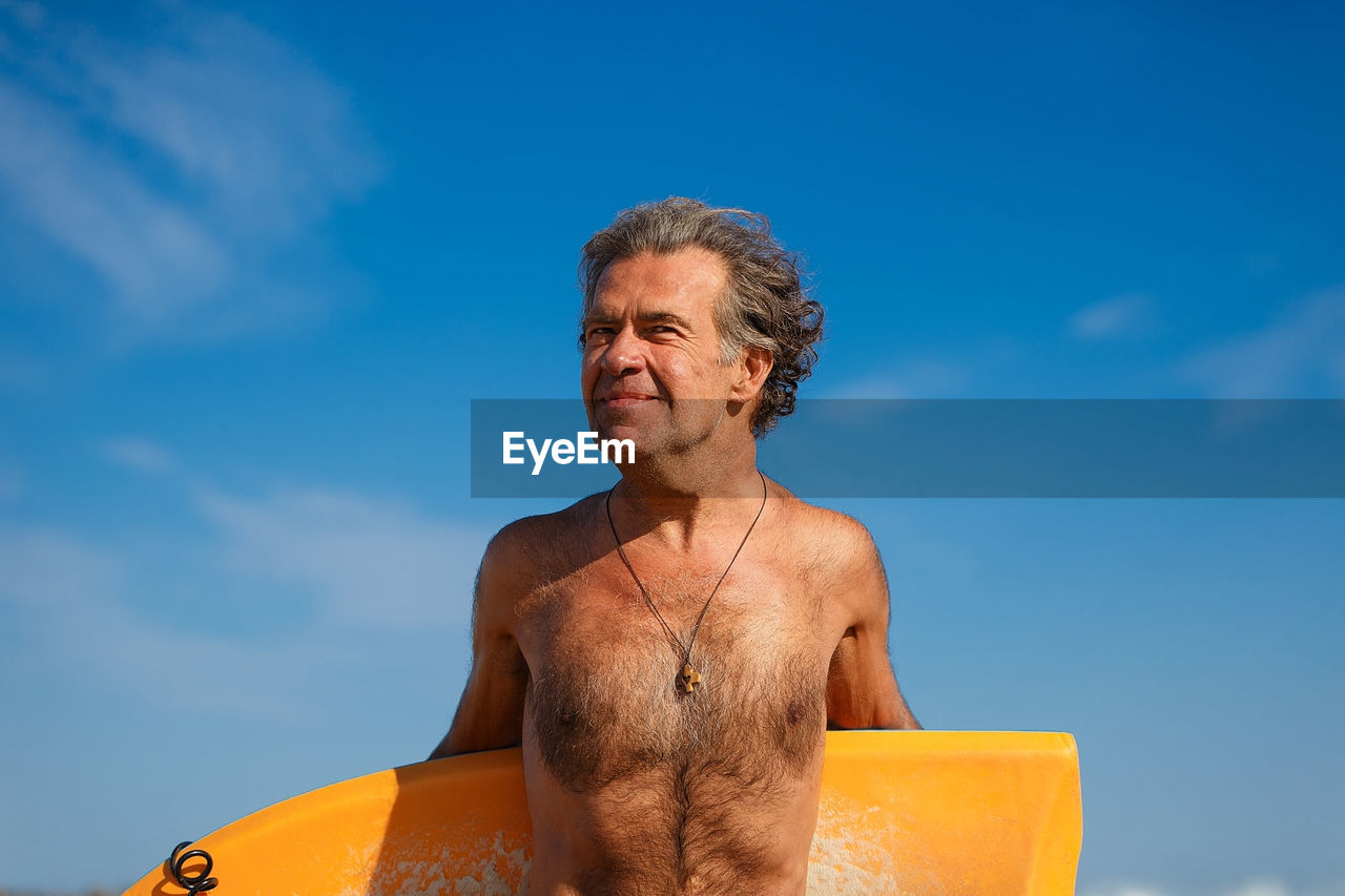 Close-up of shirtless man against blue sky