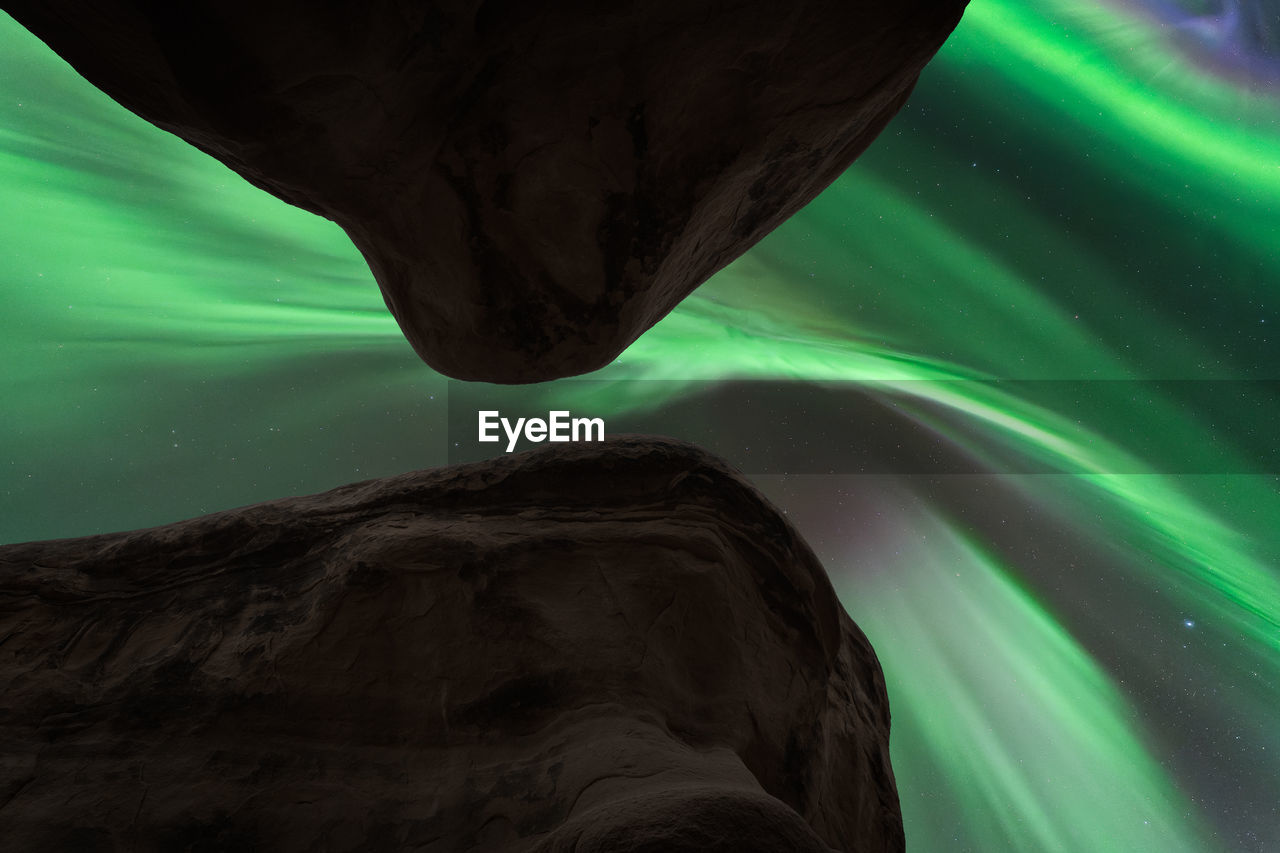 Through hole in rocky mountains view of dark night sky with glowing green polar lights in norway