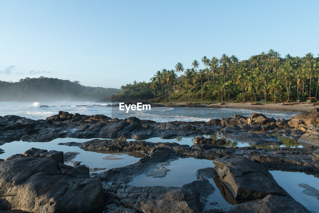 Scenic view of rocks by sea against clear sky