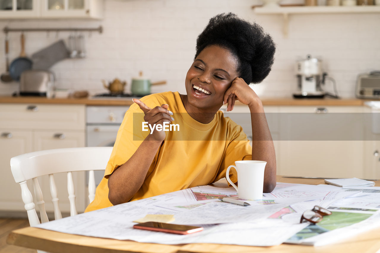 Overjoyed black businesswoman laugh work from home. cheerful architect sit at table with blueprints