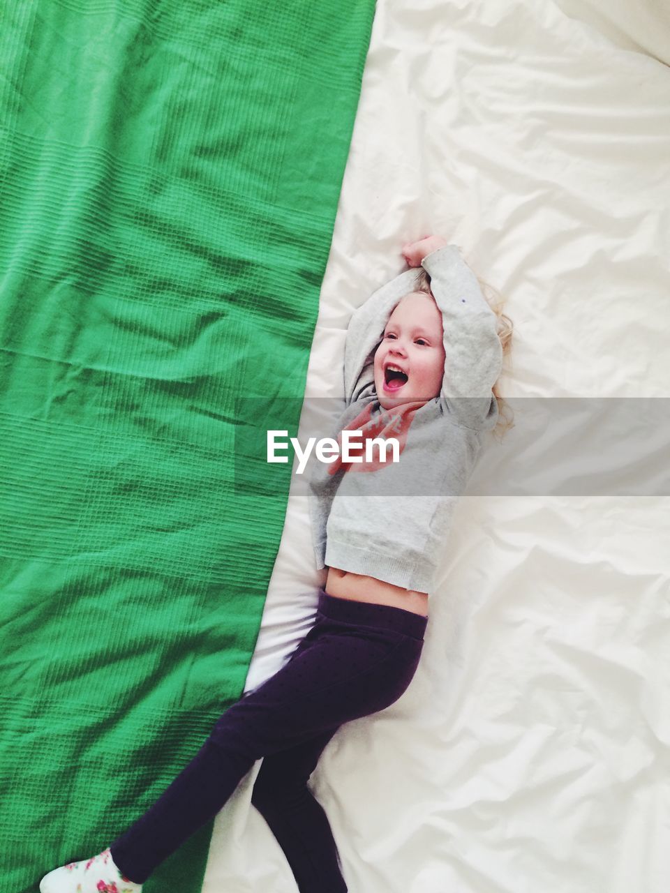 High angle view of cheerful girl lying on bed at home