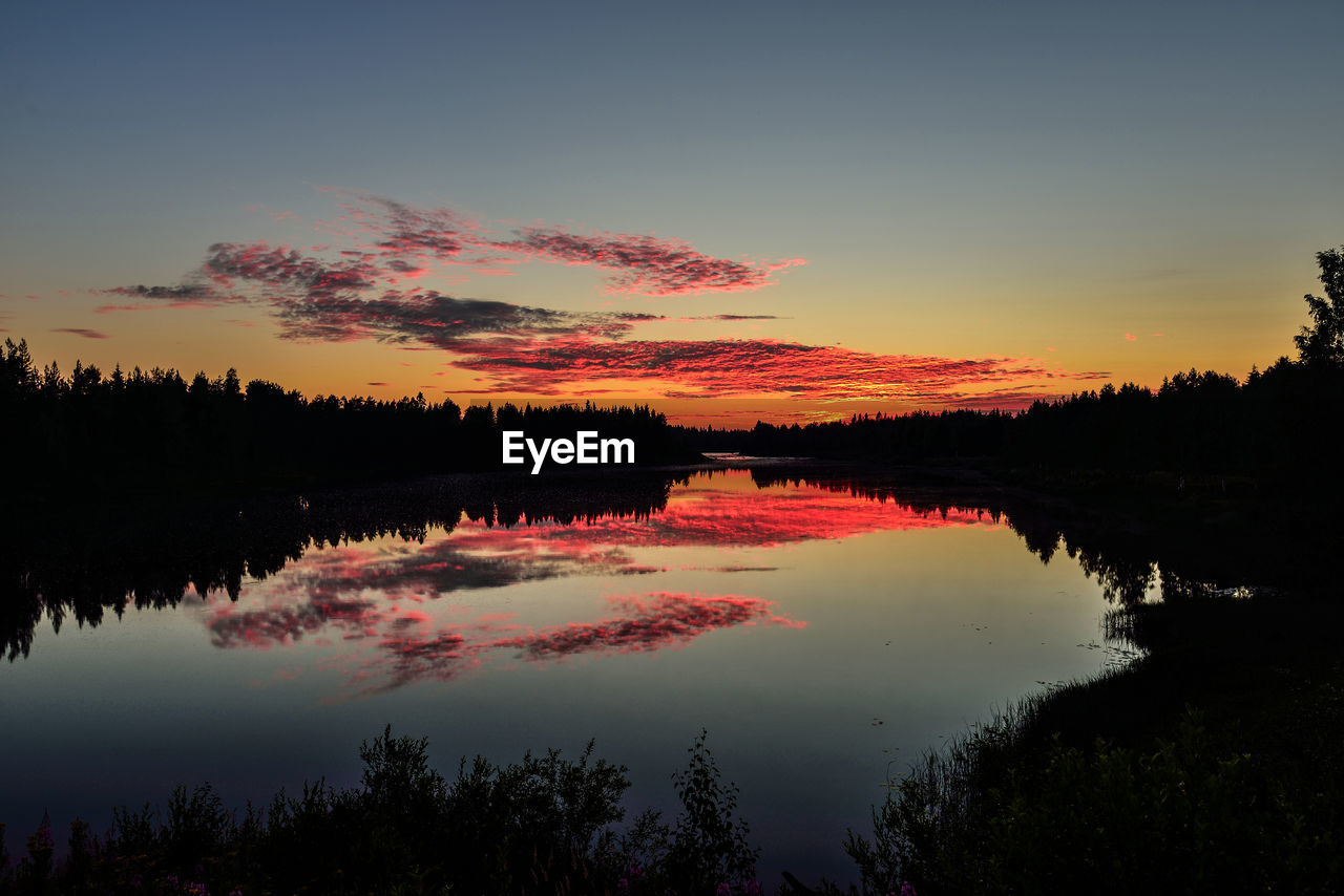 REFLECTION OF SILHOUETTE TREES IN LAKE AGAINST SKY DURING SUNSET