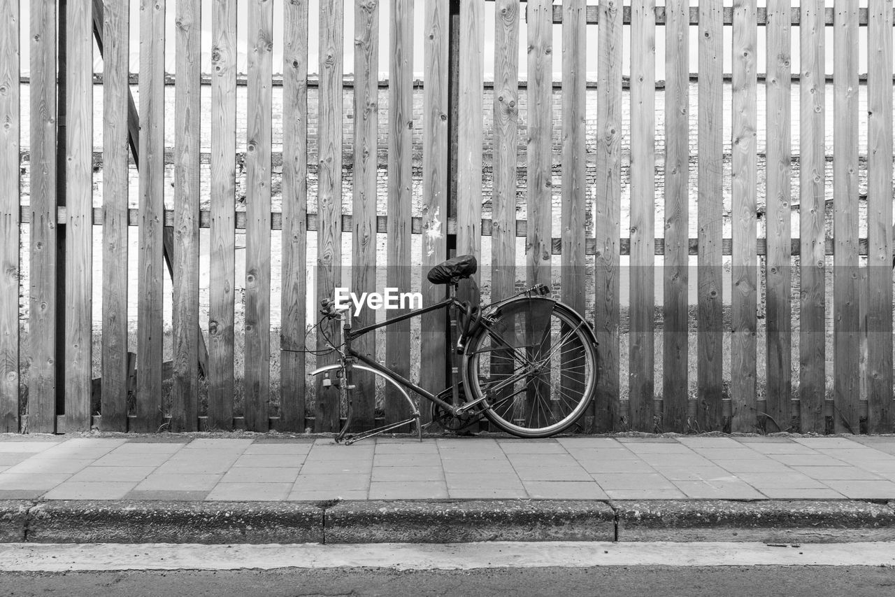 Damaged bicycle leaning on wooden fence