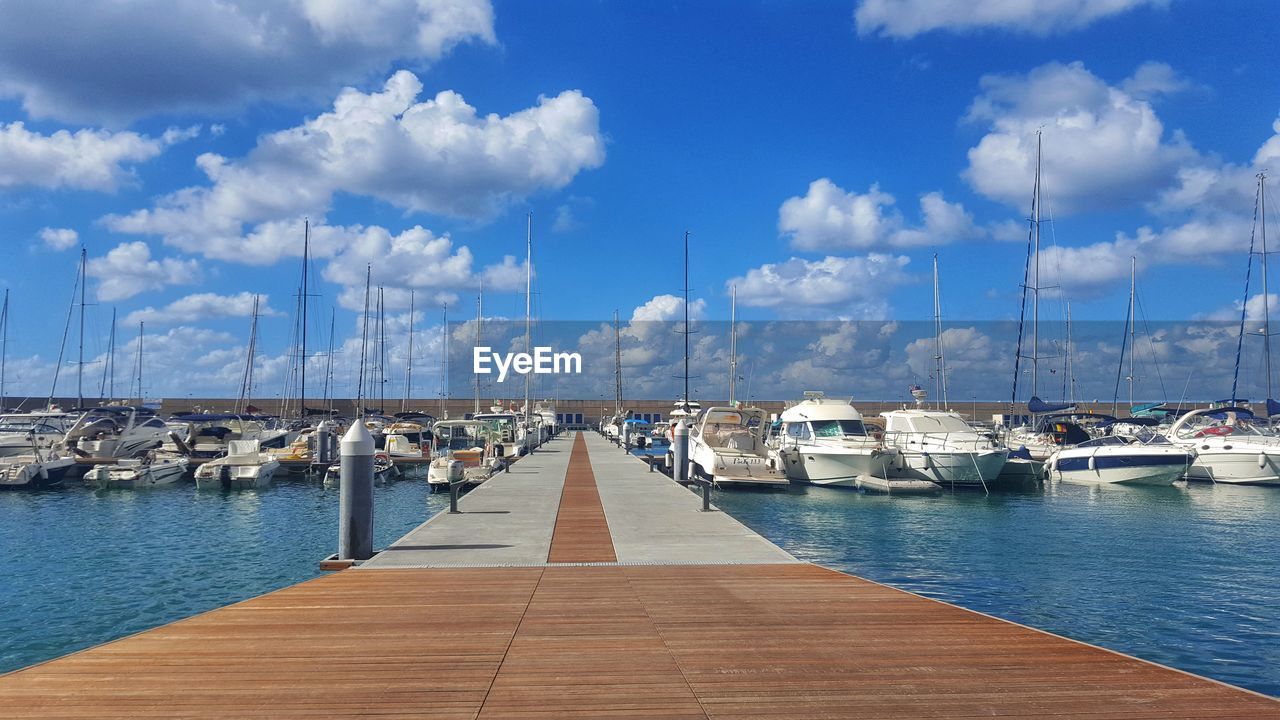 Sailboats moored at harbor against sky