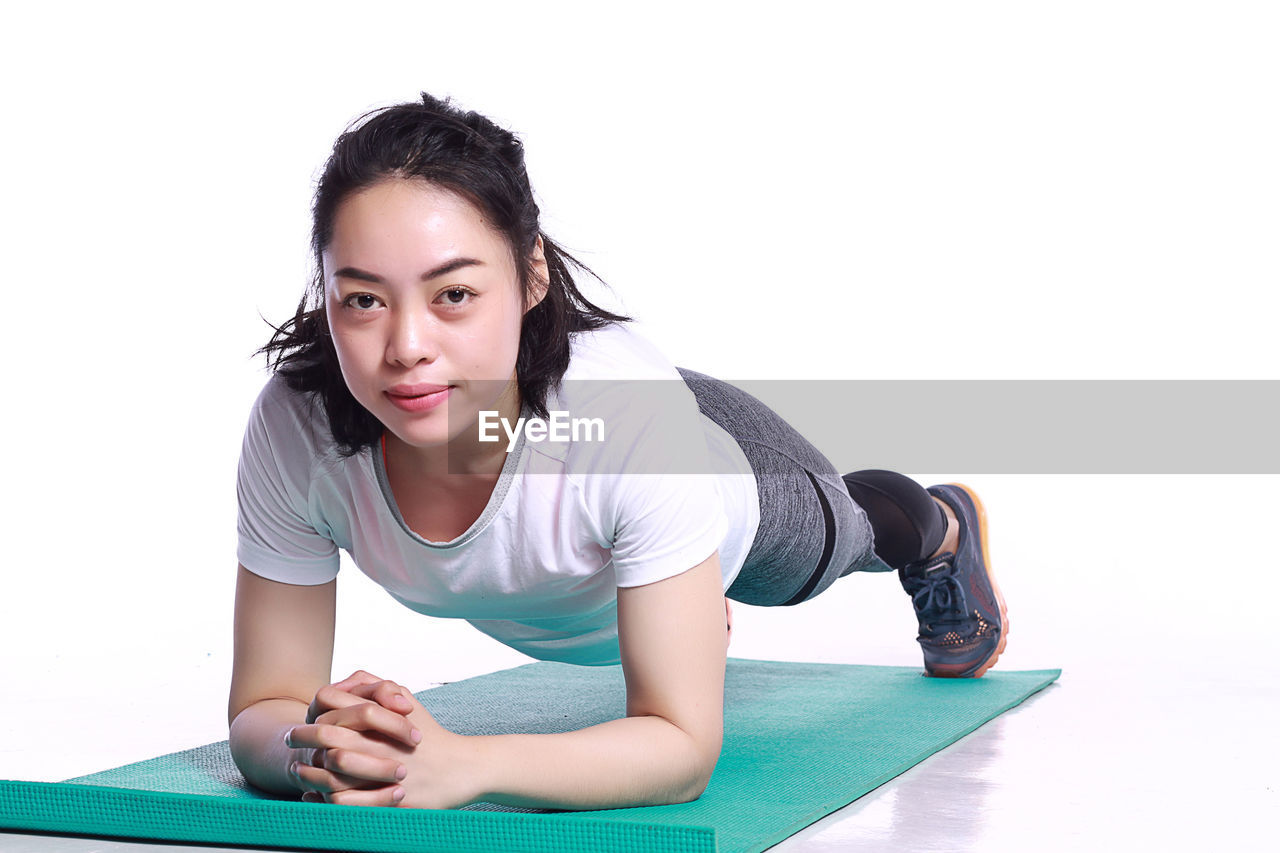 Young woman exercising on mat against white background