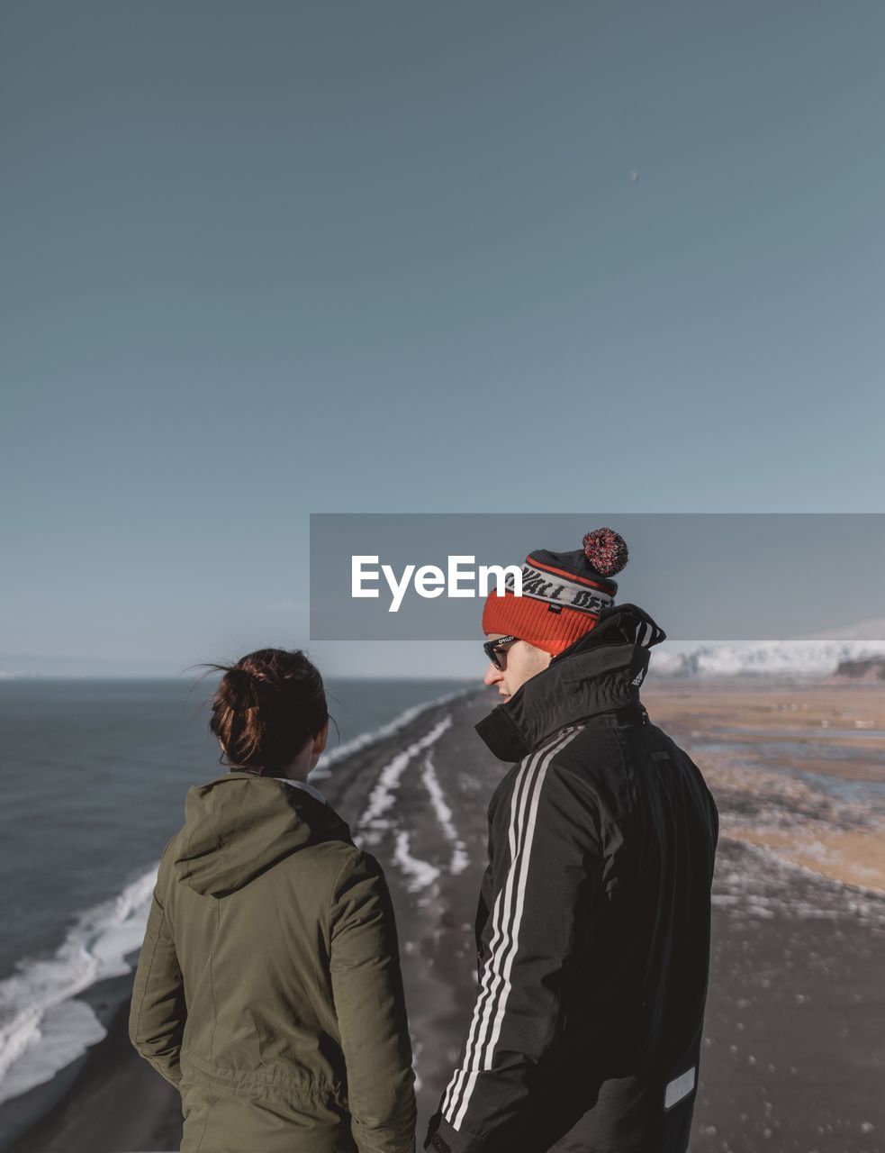 REAR VIEW OF PEOPLE STANDING ON BEACH