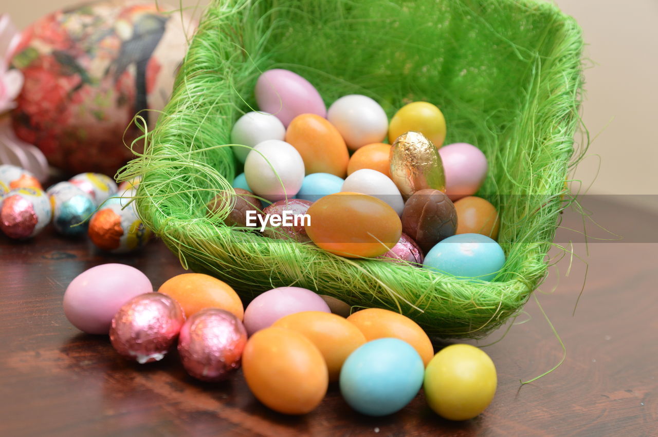 CLOSE-UP OF MULTI COLORED EGGS IN BASKET ON TABLE