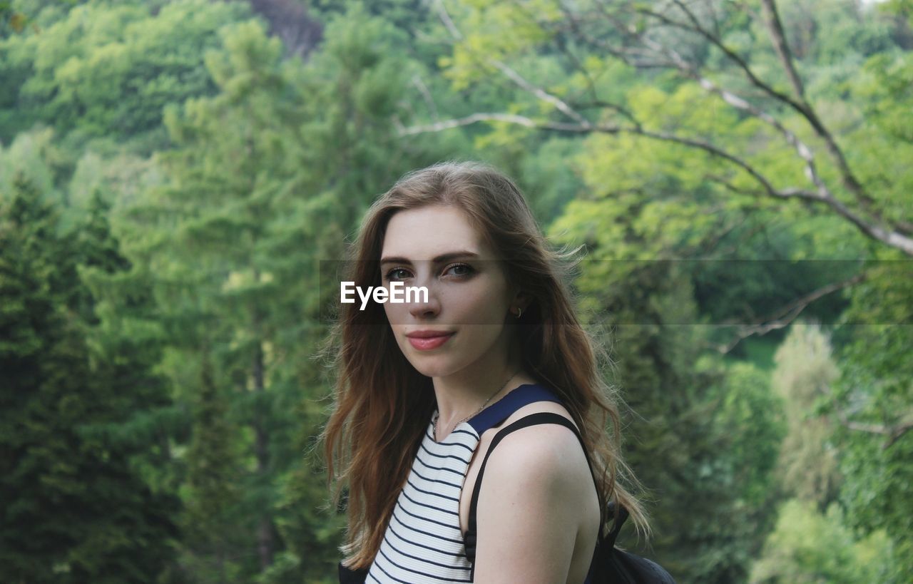 Portrait of beautiful young woman standing against trees