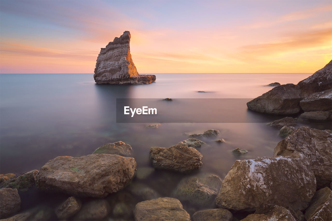 Rocks on sea against sky during sunset