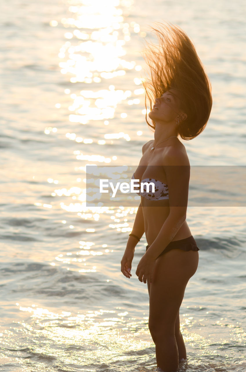 Sensuous woman in bikini tossing hair while standing in sea