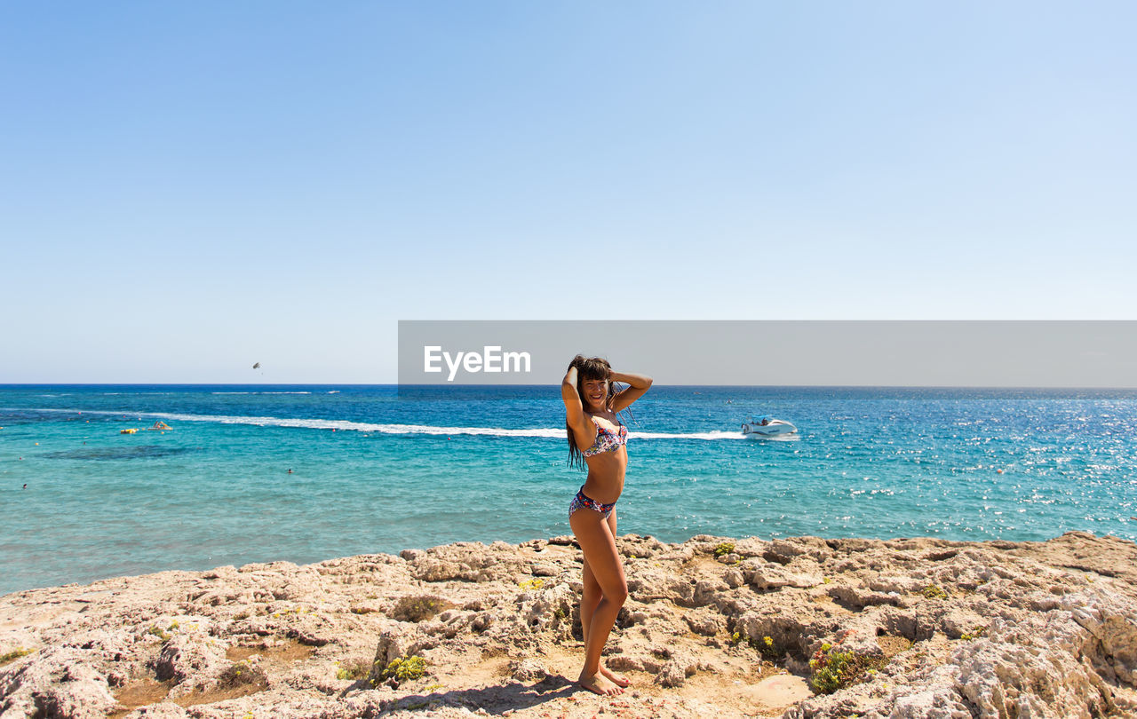 FULL LENGTH OF YOUNG WOMAN STANDING ON BEACH