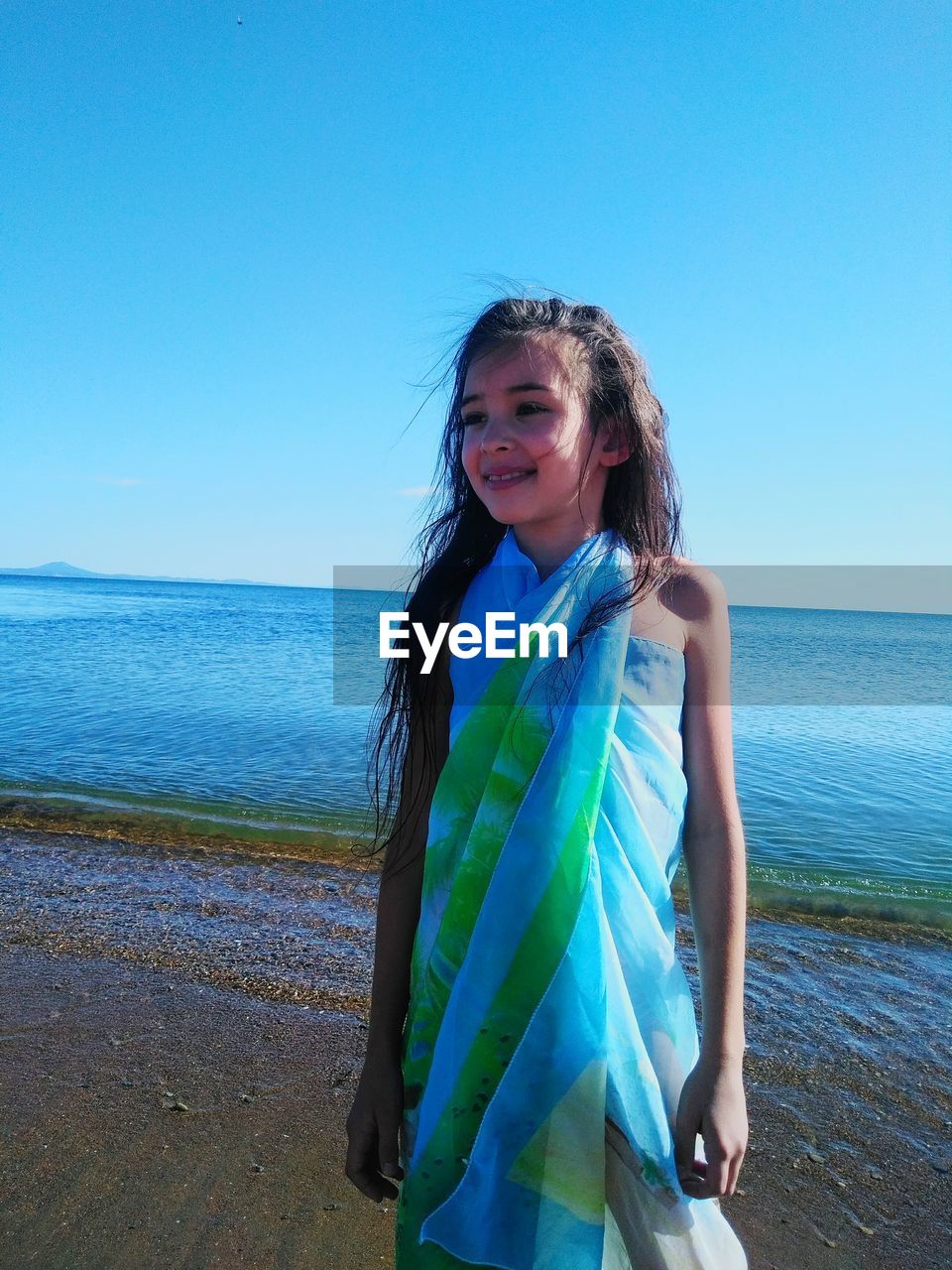 Girl covered with sarong standing on shore at beach 