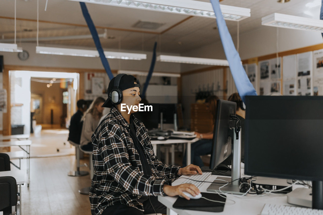 Young man using computer while listening through headphones in lab