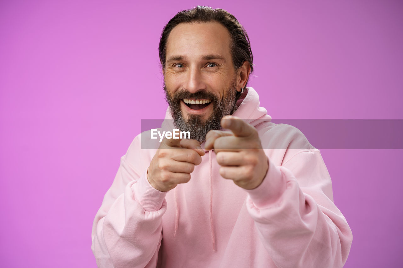 Portrait of smiling man holding pink face against gray background