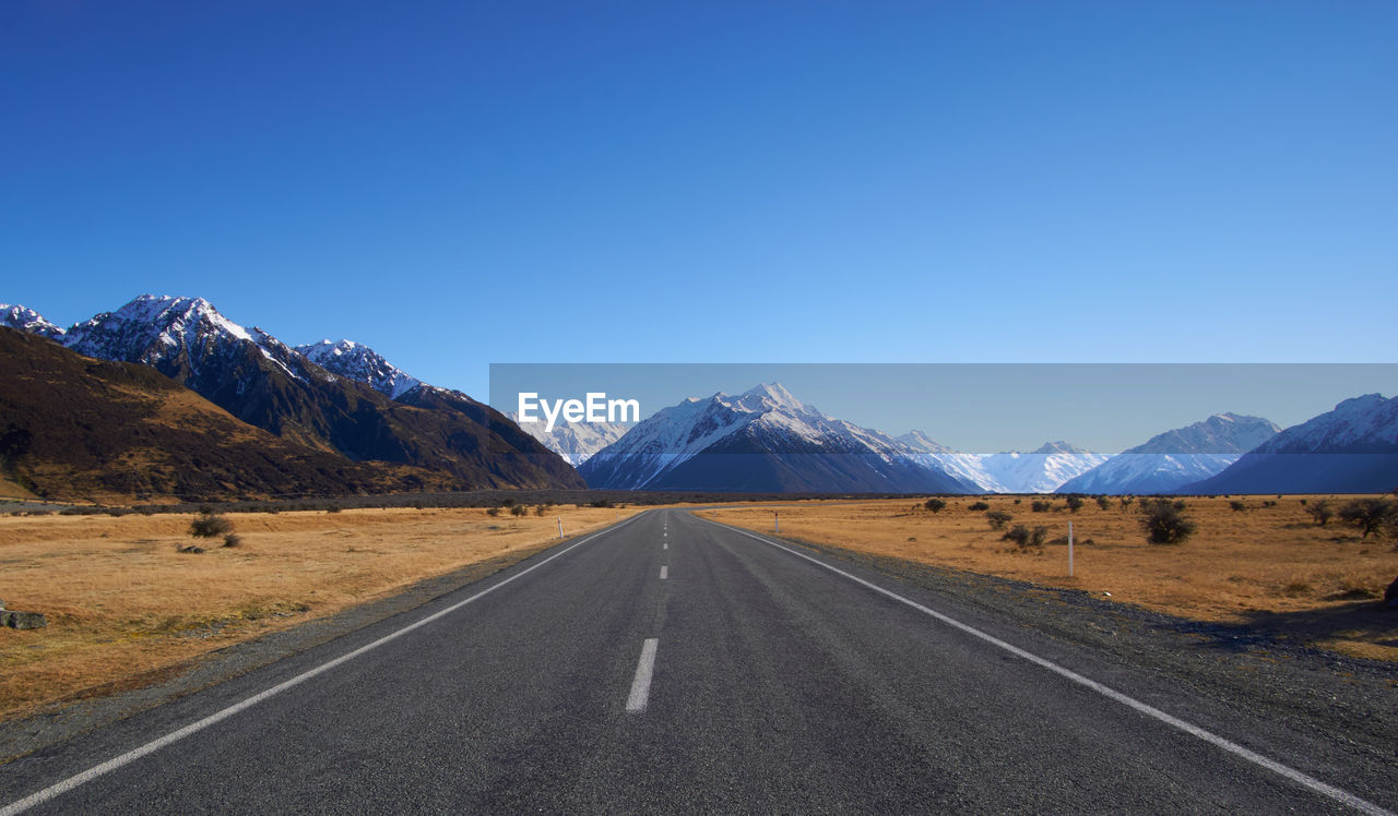 Road leading towards snow covered mountains against clear sky