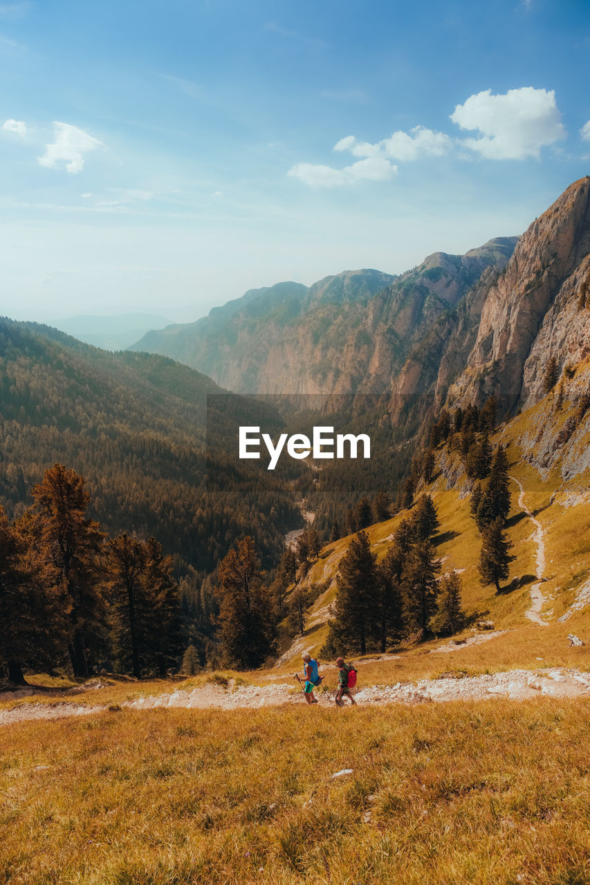 Rear view of people walking hiking on field and trail with mountains in background on sunset