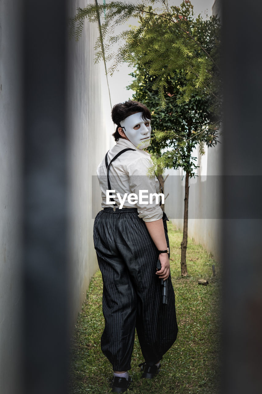 Portrait of a person wearing a mask behind a black gate walking away holding a fake gun