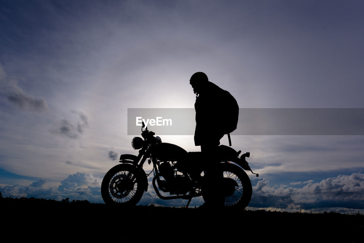 Silhouette biker with motorcycle standing on landscape against sky during sunset