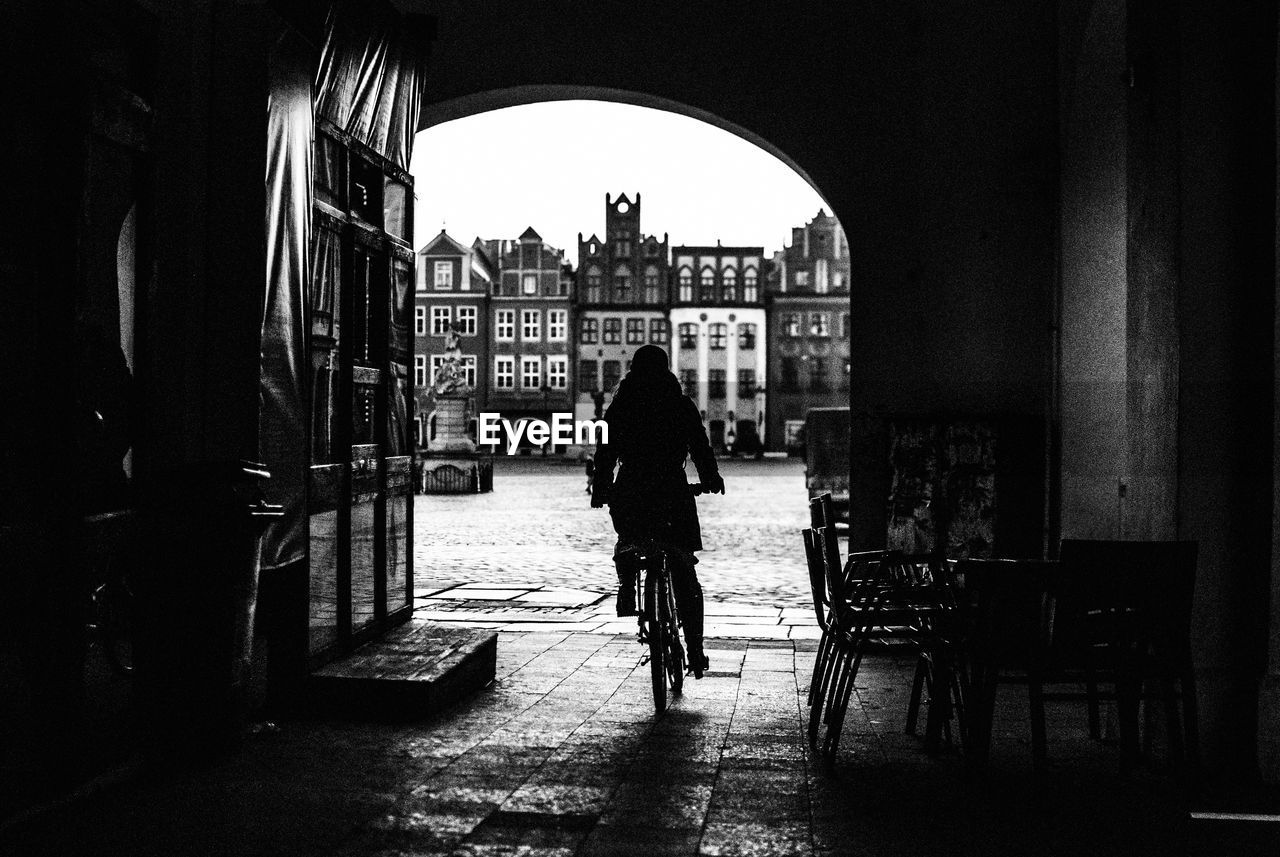 Silhouette person riding bicycle on street against buildings