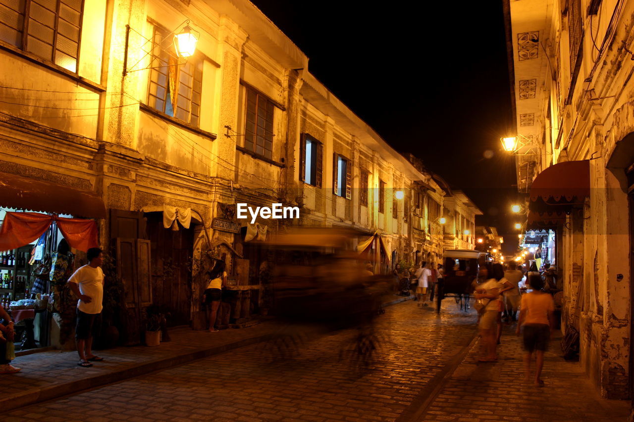 People on street amidst old buildings in city at night