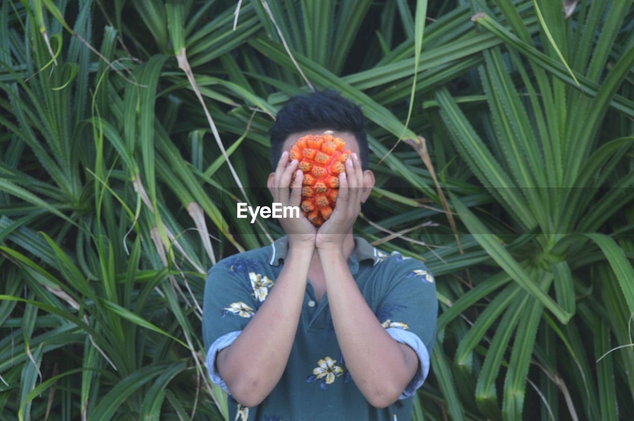 Man holding fruit in front of face against plants