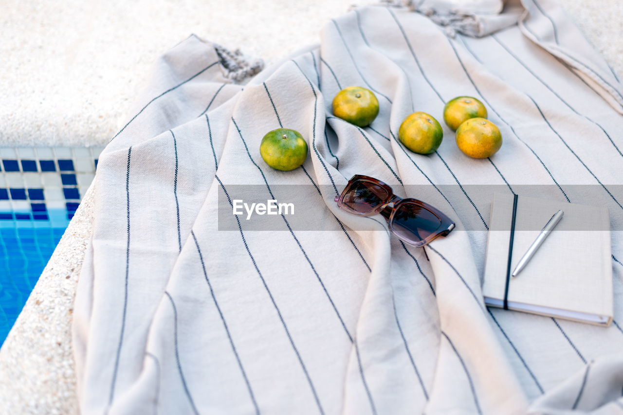 Sunglasses, notebook, pen, and tangerines lie on a picnic blanket by the pool. summer concept.