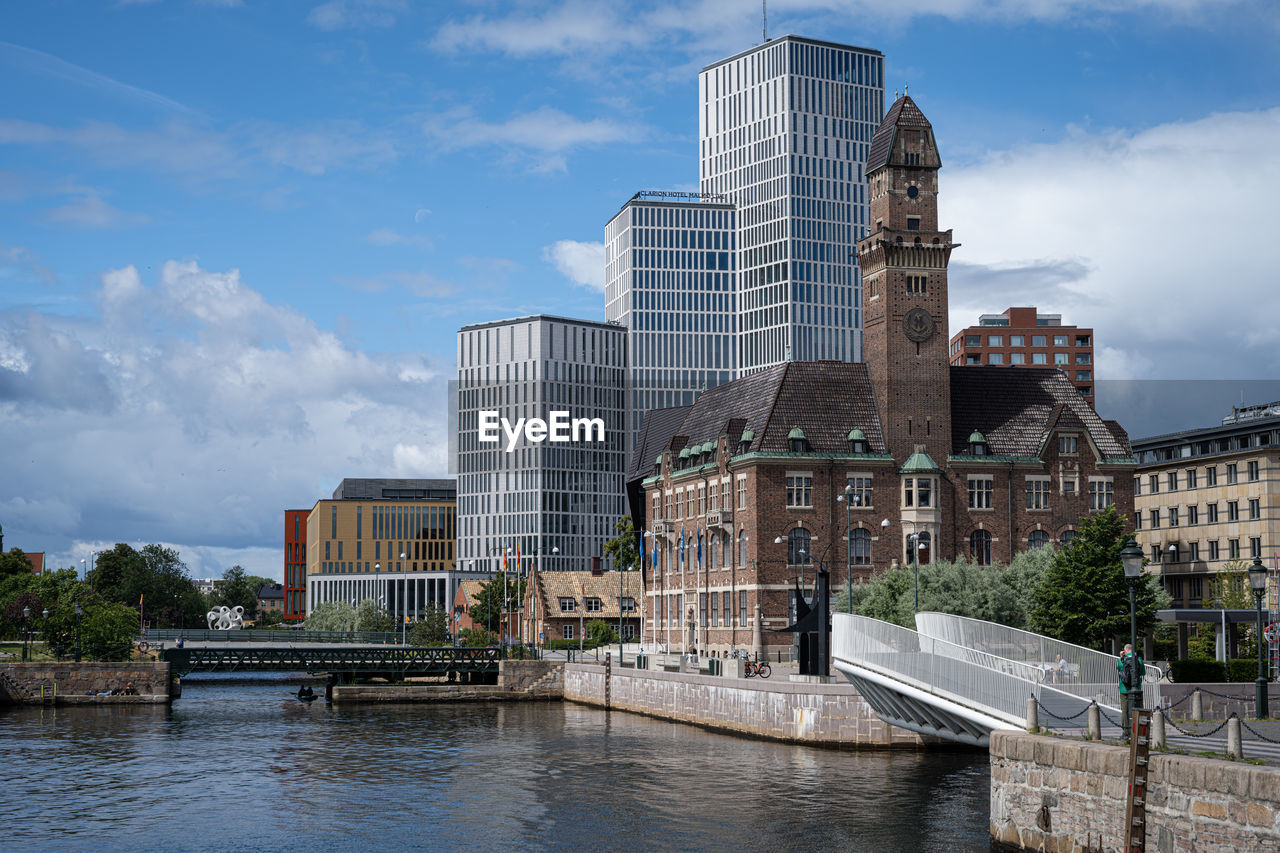 Bridge over canal by tall buildings against sky