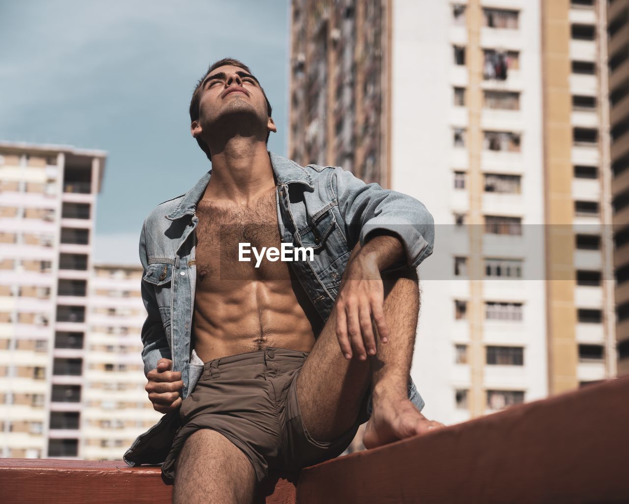 MIDSECTION OF MAN LOOKING AWAY AGAINST CITY BUILDINGS