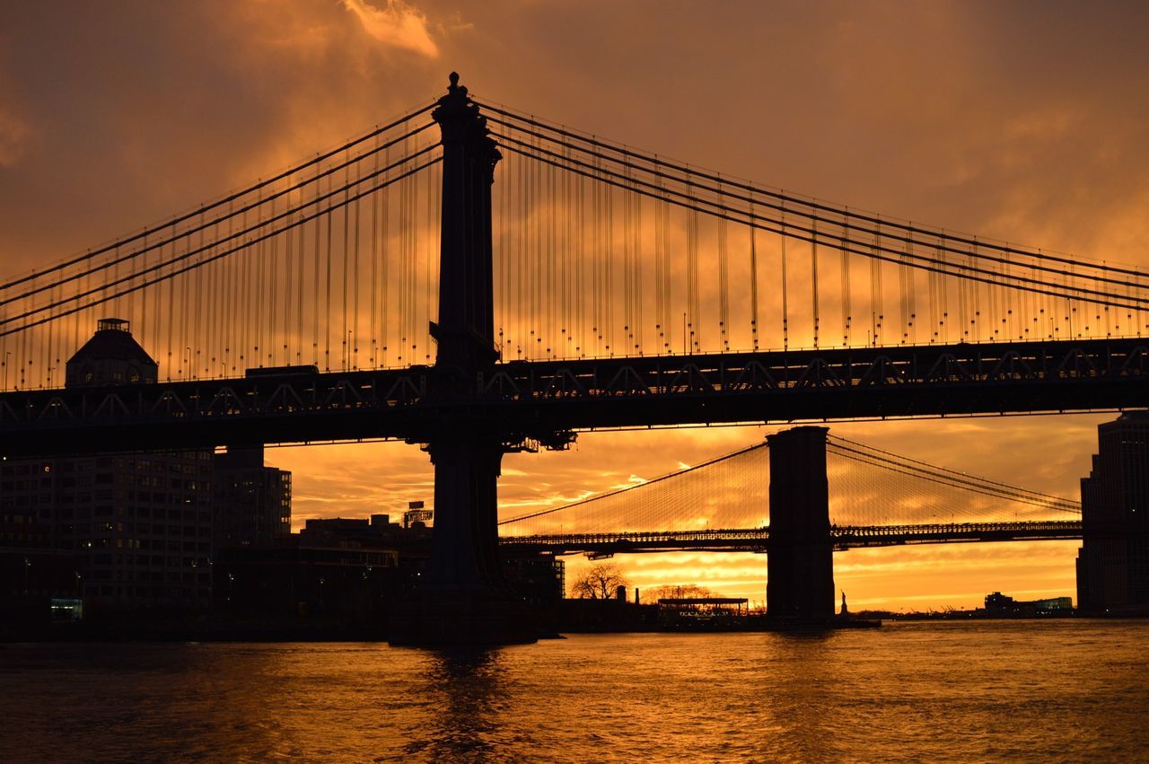 Low angle view of silhouette brooklyn bridge over river against orange sky