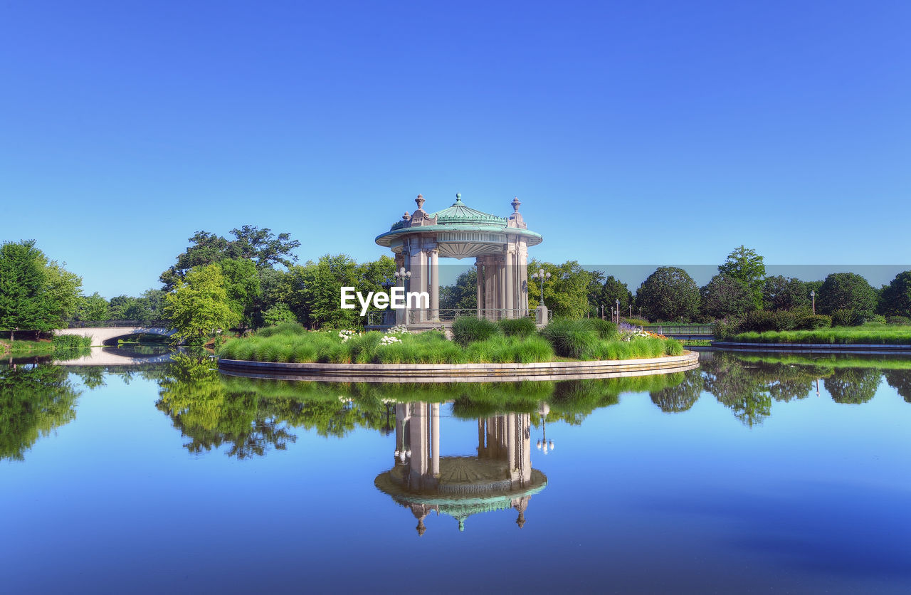 Reflection of building in lake against clear blue sky