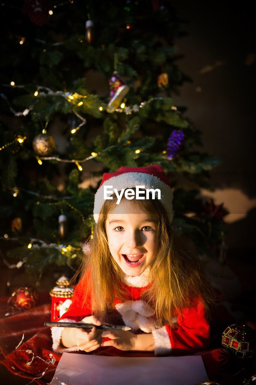 Cute girl lying down by illuminated christmas tree