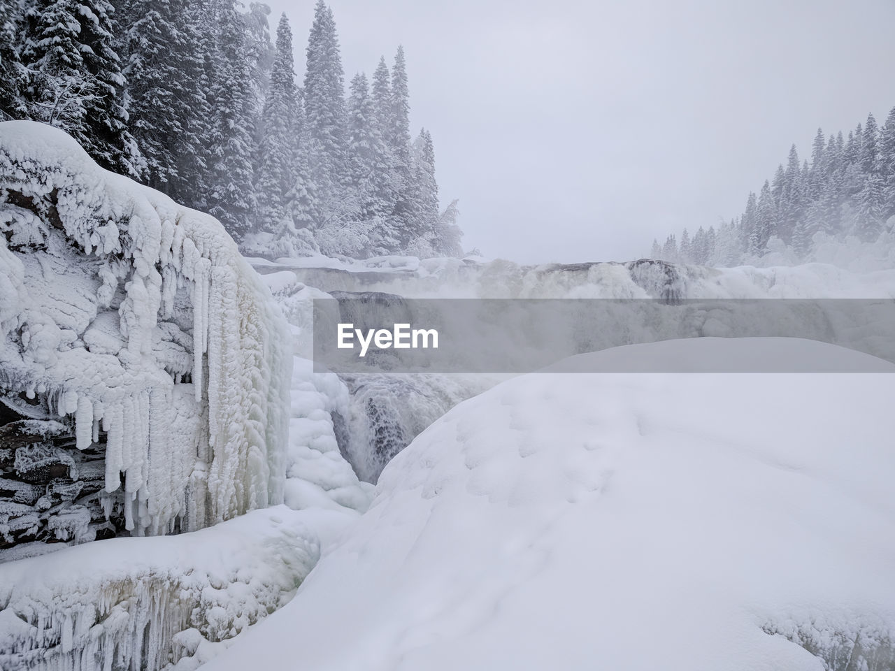 Snowy landscape surrounding icy waterfall