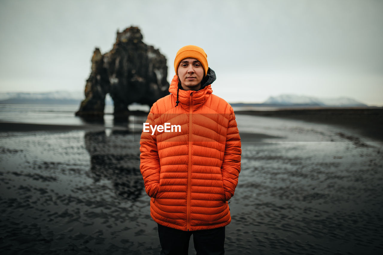 Young tourist near land in water and big stone cliff on blurred background