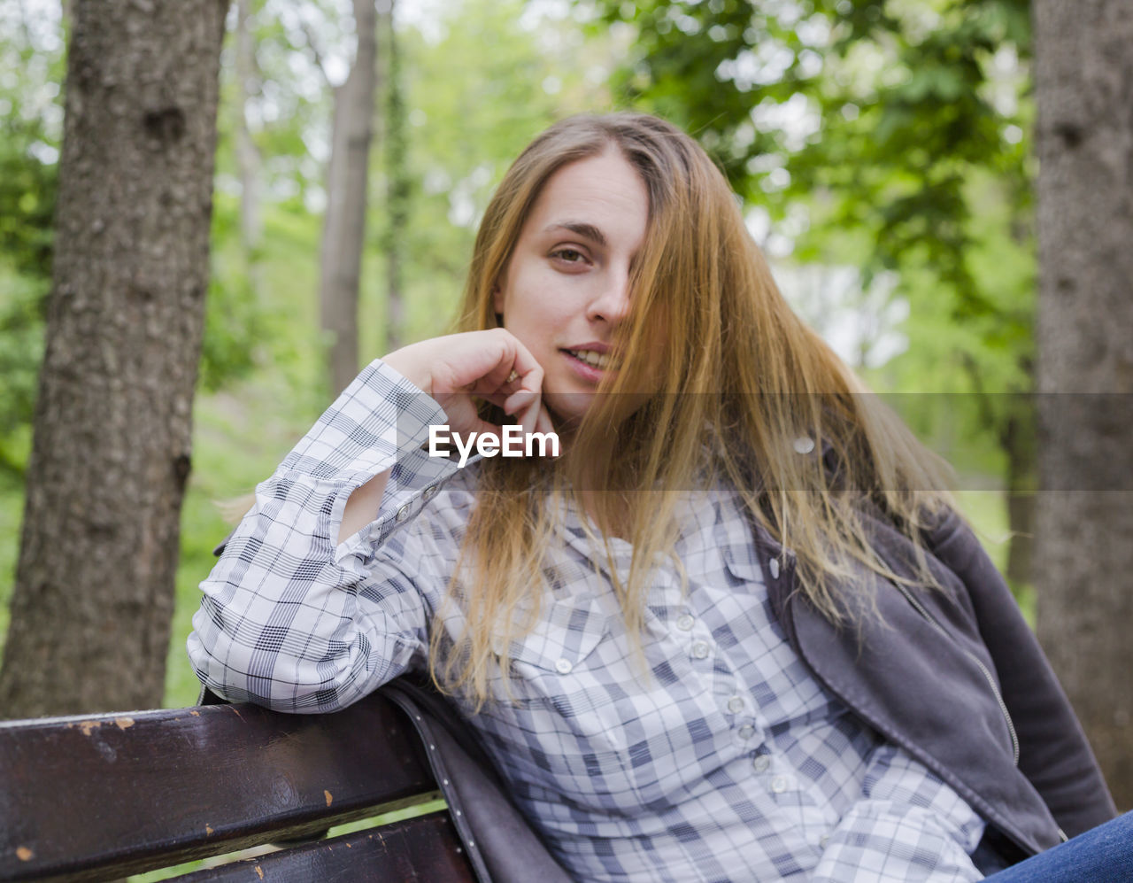 Portrait of woman sitting on bench against trees in forest