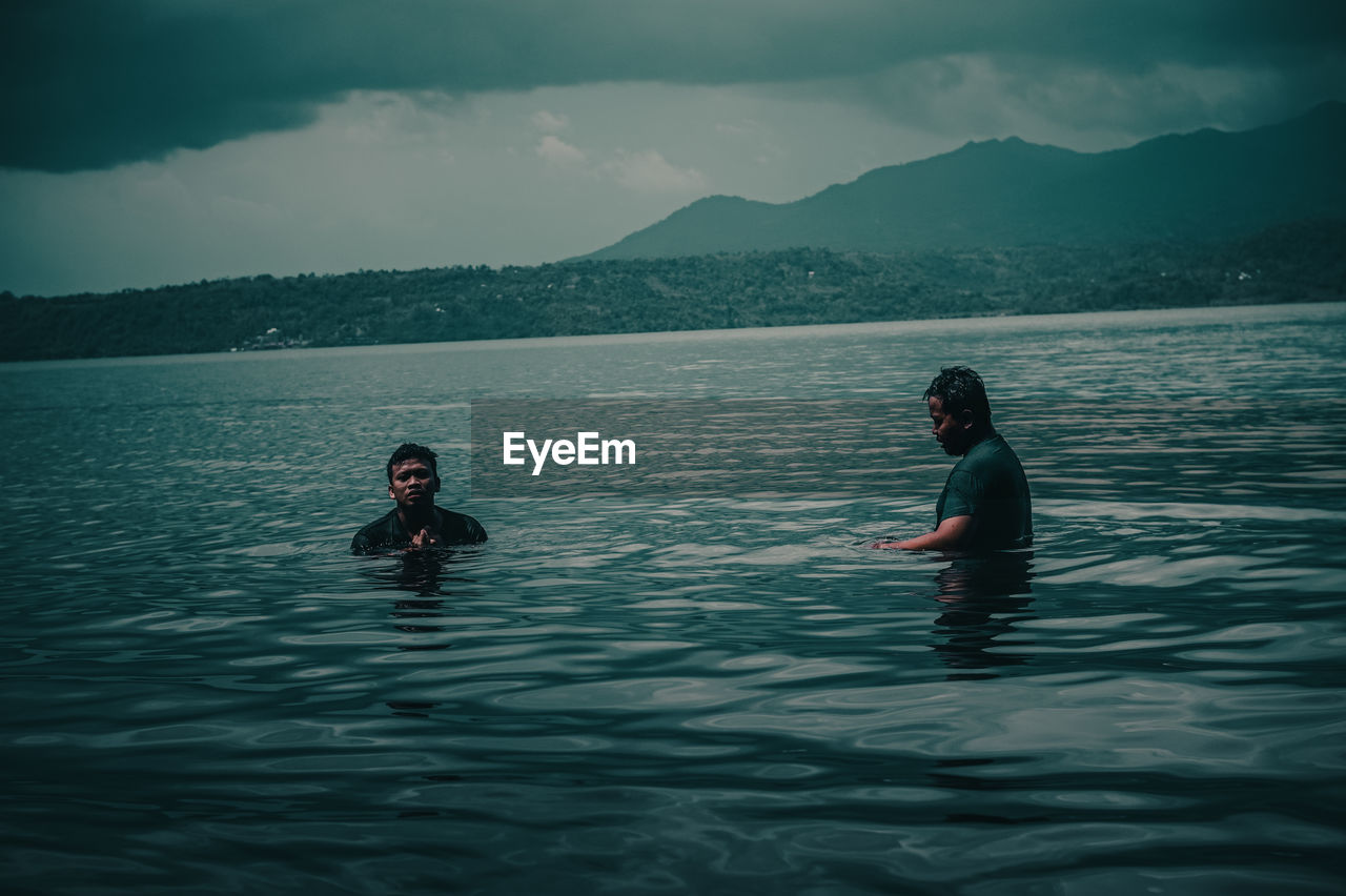 Asian men swimming in lake ranau with mountain views, ranau indonesia.