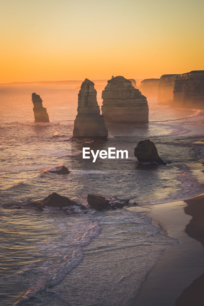 Rock formation in sea against sky during sunset