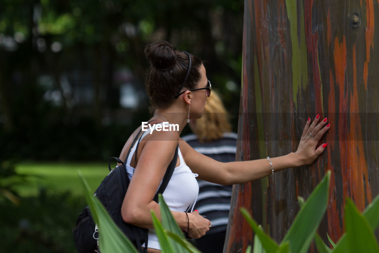 Side view of woman standing touching while standing by painted tree trunk