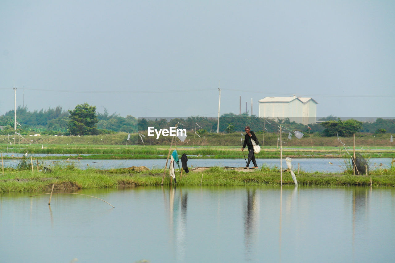 Side view of man walking on lake against clear sky